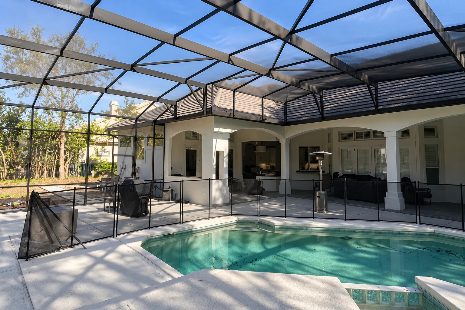 Screened patio enclosure surrounds a backyard pool, with black framing and a mesh safety fence beside the house.