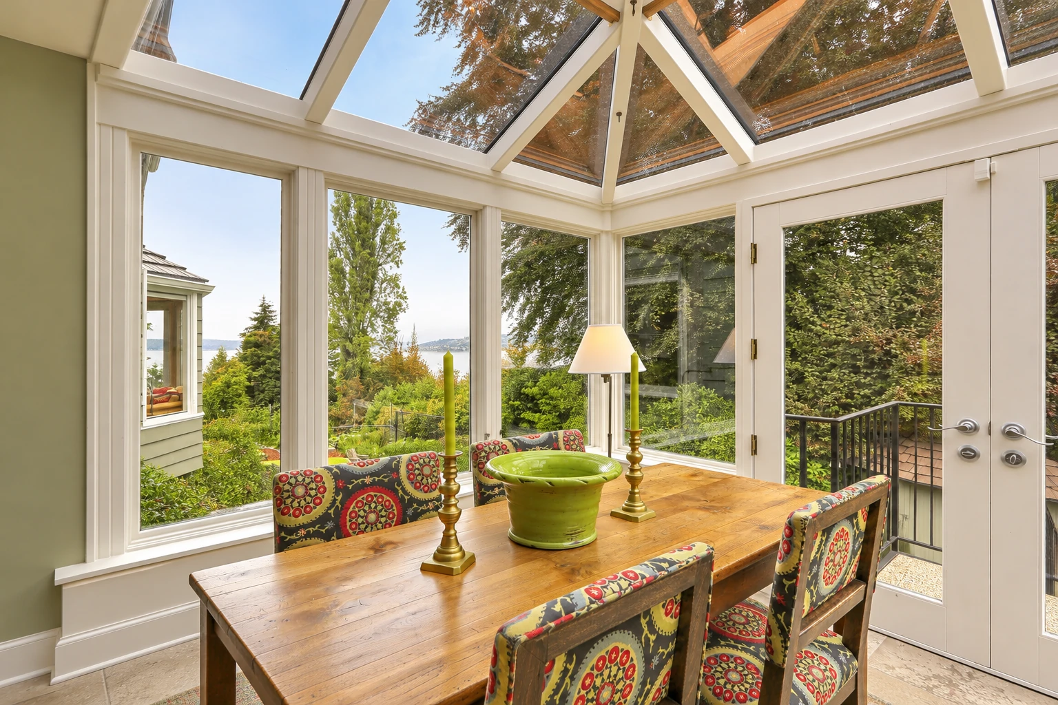 Bright sunroom with a glass-paneled roof, large windows, and a wooden dining table with patterned chairs.